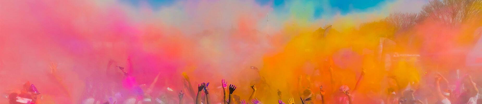 A crowd of people throwing coloured powder in the air at Holi Festival