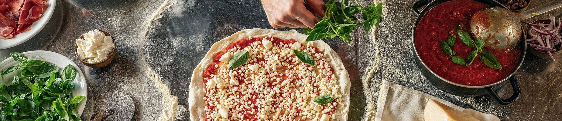 A person decorating a pizza with ingredients