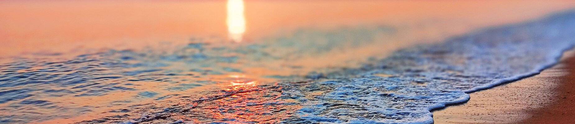 A wave crashing against the shore with a backdrop of the sun setting