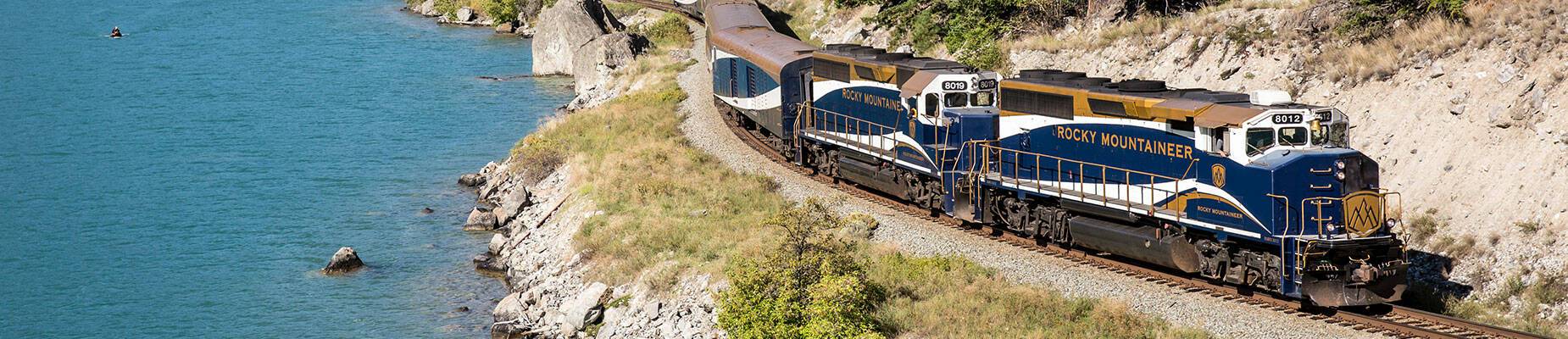 Rocky Mountaineer travelling along tracks next to a lake
