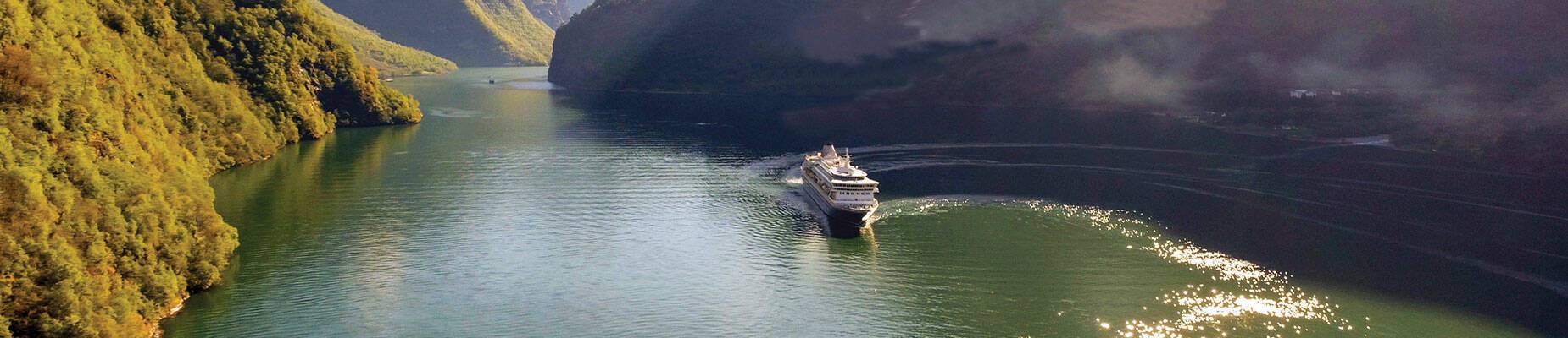 A cruise ship sailing through a sunny Norwegian fjord