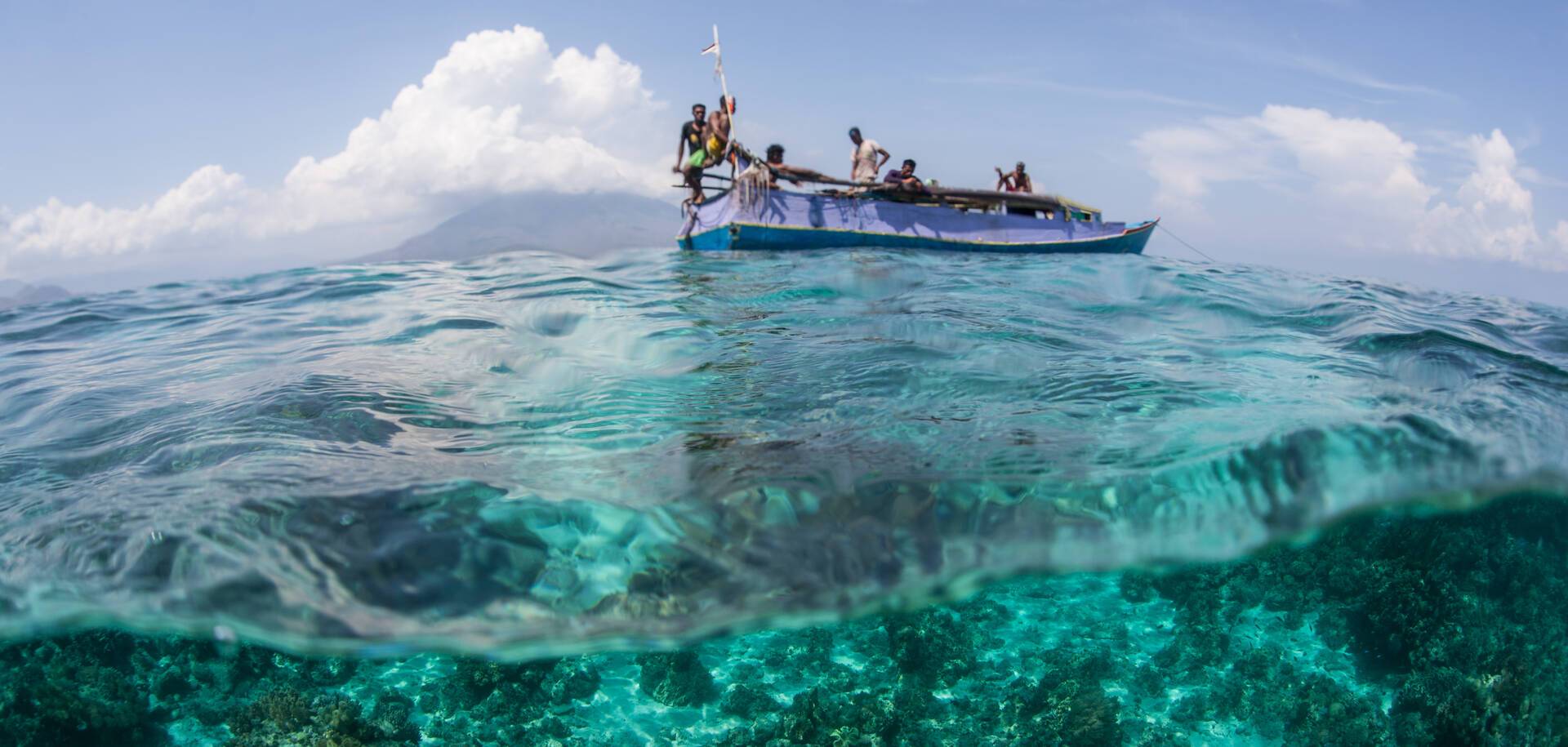 Indonesian fishermen, from the island of Flores, sit on their boat near a coral reef